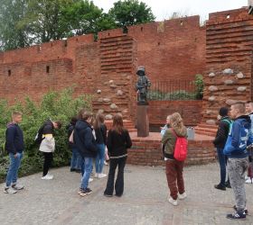 Uczniowie klasy 8a stoją przed pomnikiem Małego Powstańca i słuchają opowieści przewodniczki