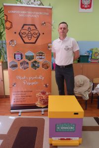 1. Edukator pszczelarstwa stoi na tle baneru, przed nim el edukacyjny.
