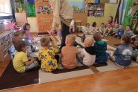 5. Edukator pokazuje dzieciom miotełkę do omiatania pszczół, dzieci siedzą w kręgu na dywanie.